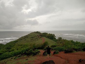 Rear view of man walking on field at mountain against cloudy sky