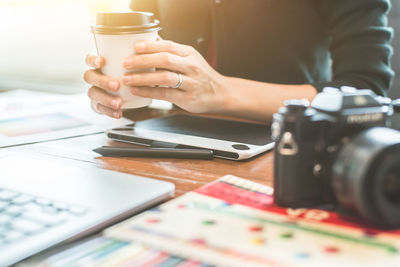 Midsection of woman holding disposable cup at table in office