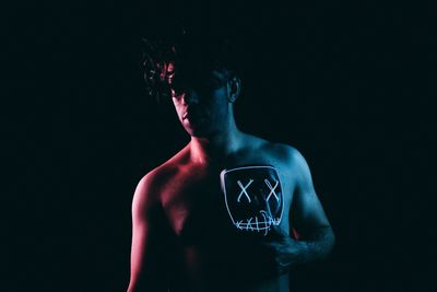 Shirtless man holding mask against black background