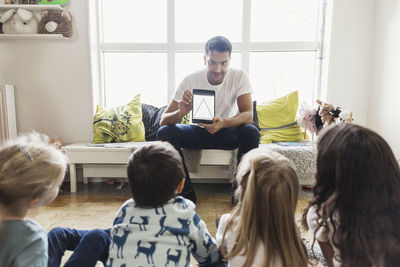 Male teacher showing triangle shape to students on digital tablet