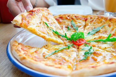 Close-up of woman hand holding pizza in plate on table