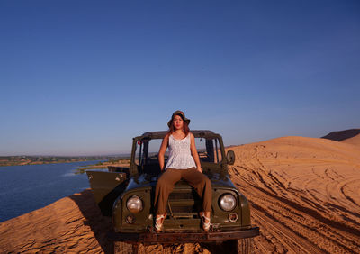 Portrait of woman sitting on off-road vehicle against clear blue sky