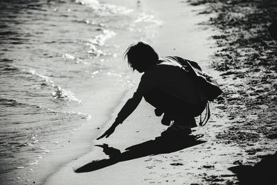 Side view of man crouching on shore at beach
