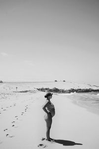Rear view of woman standing at beach against clear sky