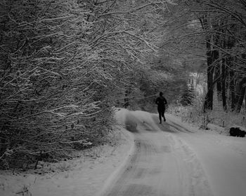 Rear view of man running on snow covered road