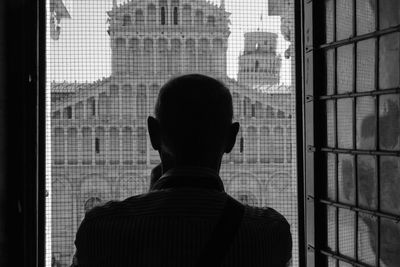 Rear view of silhouette man looking through window