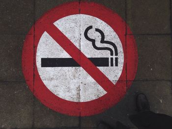 Low section of man standing by no smoking sign on footpath