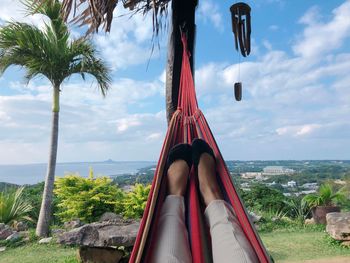 Low section of woman relaxing in hammock against sky