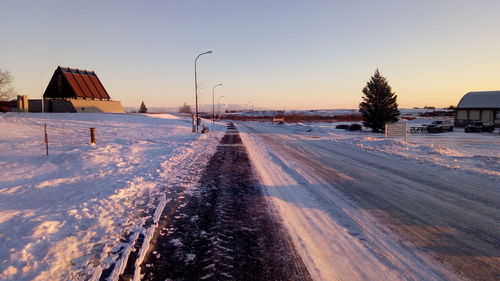 Snow covered road by buildings against sky during winter