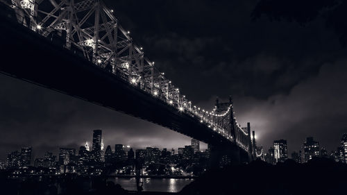 Illuminated brooklyn bridge against the cloudy sky at night