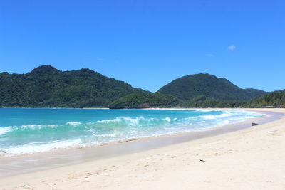Scenic view of beach and mountains against clear blue sky