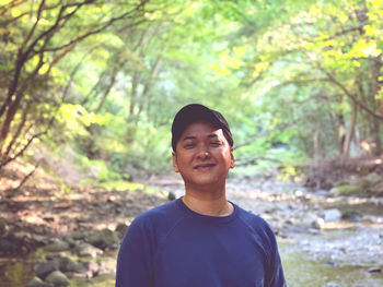 Portrait of young man standing against trees in forest