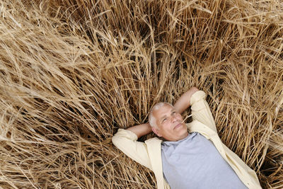 Senior man with hands behind head resting on wheat field