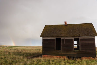 Abandoned cottage on field against cloudy sky