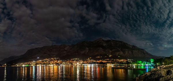 Illuminated buildings by sea against sky at night