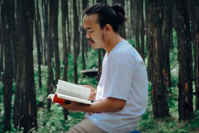 Side view of teenage girl holding tree trunk in forest