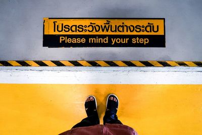 Low section of person standing on yellow sign