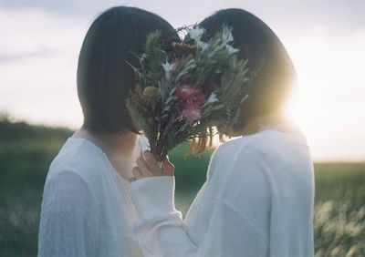 Portrait of woman holding white flowering plant against sky
