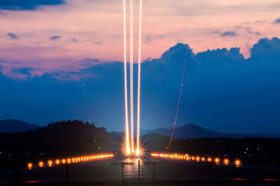 Light trail over airport runway against cloudy sky at dusk