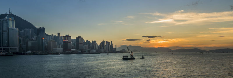 Sailboats in sea by buildings against sky during sunset