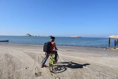 Rear view of man riding bicycle on beach