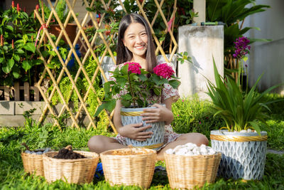 Young woman holding basket while sitting by plants