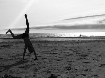 Full length of boy doing handstand at beach against sky