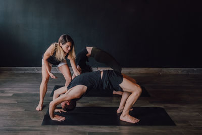 High angle of adult barefooted instructor in sportswear supporting man while teaching group of sporty people to do urdhva dhanurasana pose in contemporary workout room