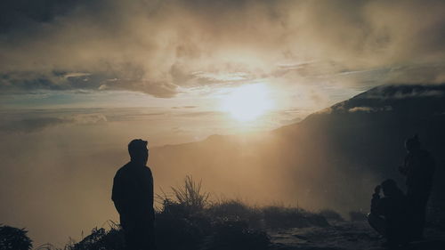 Rear view of silhouette man standing on mountain against sky