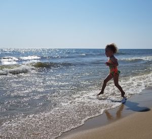 Side view of girl running in sea against clear sky during sunny day