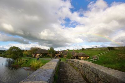 Footpath leading towards trees against cloudy sky