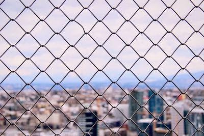 Cityscape seen through chainlink fence against sky
