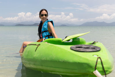 Portrait of smiling woman sitting on kayak in the sea against sky