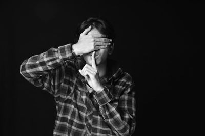 Portrait of man covering face against black background