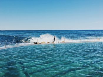 People standing on beach against clear blue sky