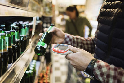 Midsection of male customer scanning beer bottle in supermarket