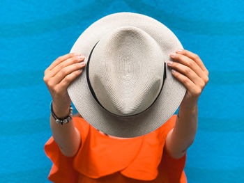 Close-up of man holding hat against blue background