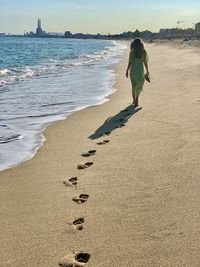 Rear view of woman on beach against sky