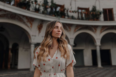 Portrait of beautiful young woman standing against built structure