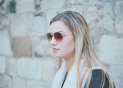 Young woman wearing sunglasses by wall