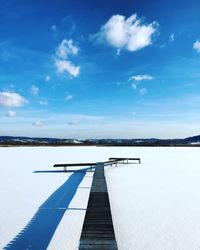 Pier on snow covered landscape against blue sky