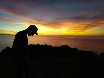 Silhouette man looking at sea against sky during sunset