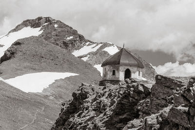 Chapel on snowcapped mountain against cloudy sky