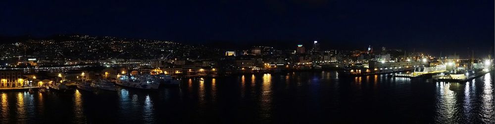 Illuminated buildings by river against sky at night