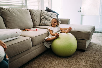 Young girl sitting on a large ball in living room looking at someone