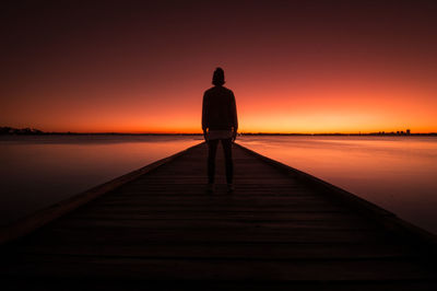 Silhouette man standing on pier over sea during sunset