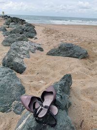 Shoes on rocks by sea against sky