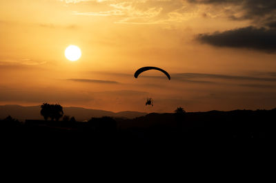 Silhouette person paragliding against orange sky during sunset