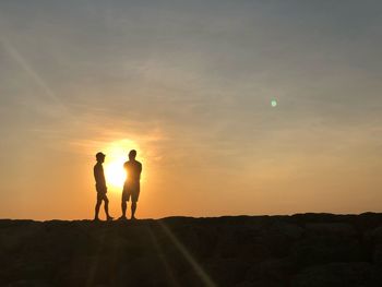 Silhouette men standing on rock against sky during sunset