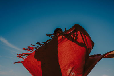 Low angle view of woman with red dress against blue sky